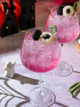 Two halloween themed Spooky Sarti Spritz cocktail drinks garnished with blackberries and blueberries in elegant tall glasses.